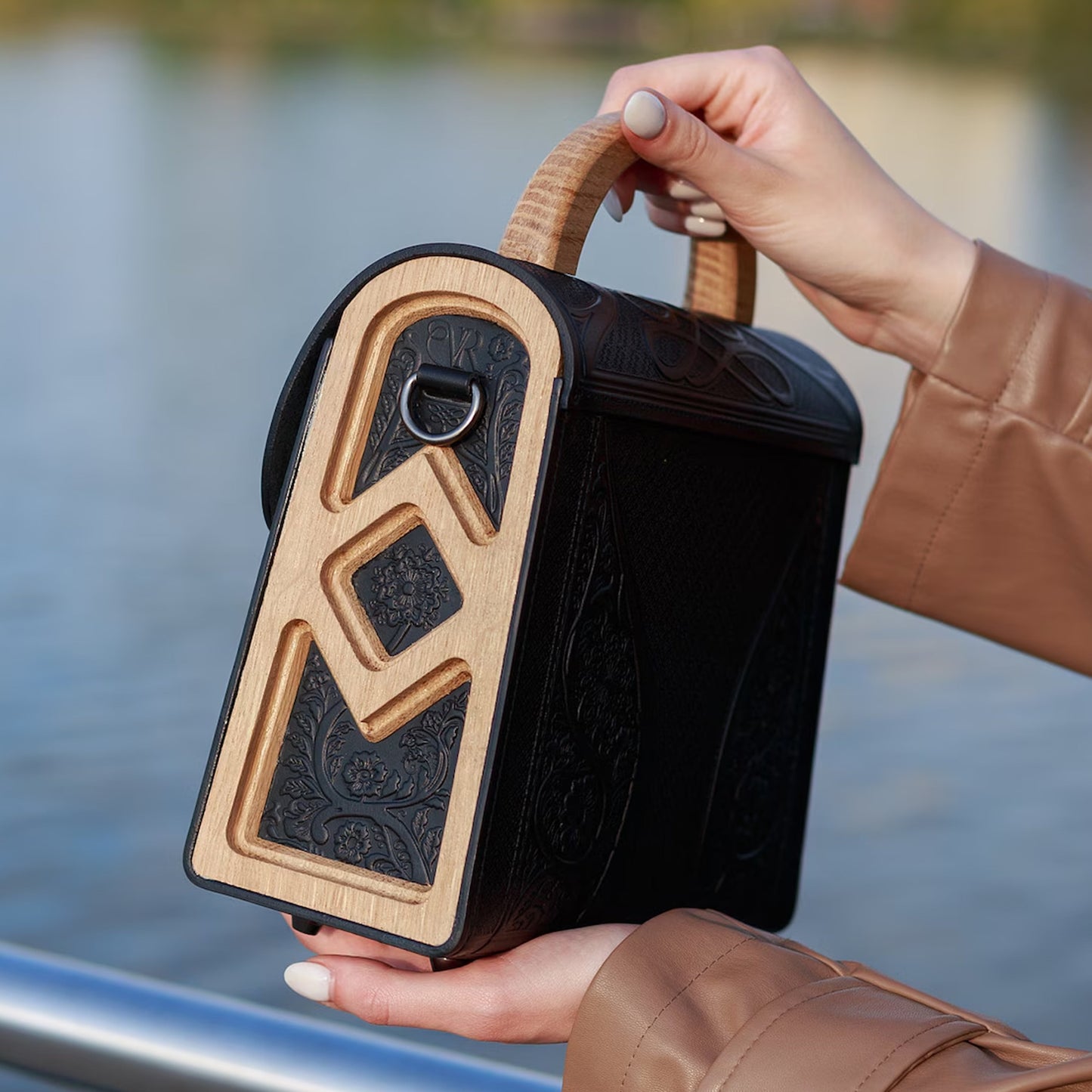 Person holding a black and wood-patterned bag by a waterfront