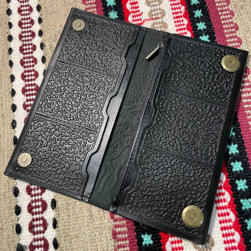 Black textured wallet with gold accents on a patterned fabric background