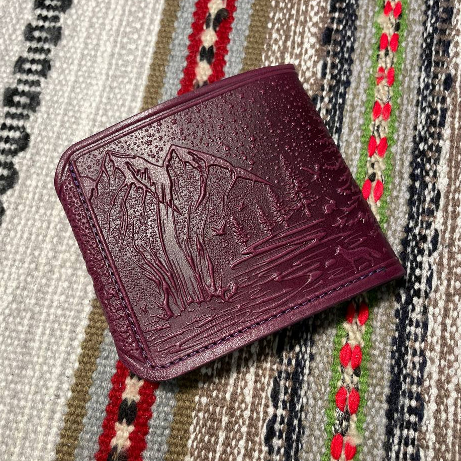 Maroon leather wallet with embossed design on a patterned fabric background