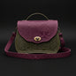 Green and purple handbag with nature-themed design on a stone surface with a garden background