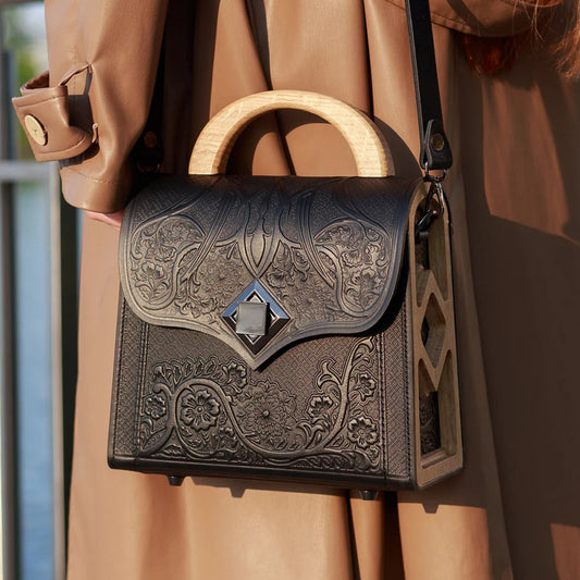Person wearing a brown coat with an ornate black handbag featuring wooden handle.