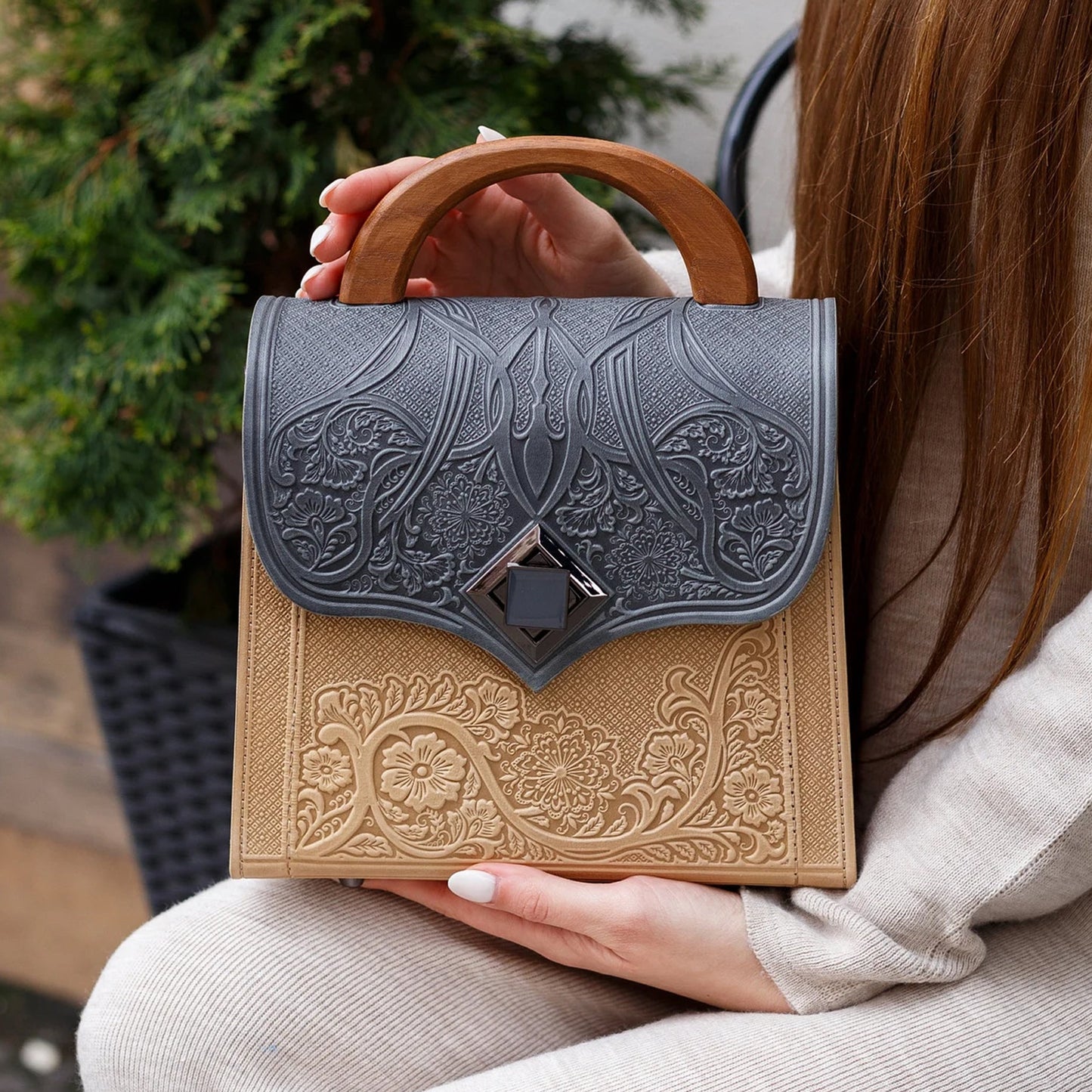 Person holding a decorative handbag with intricate designs outdoors.