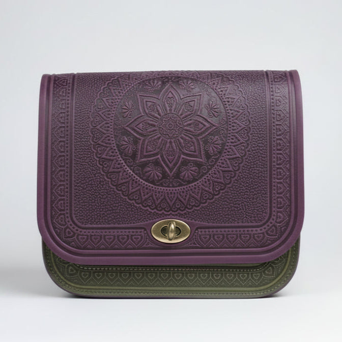 A person wearing a gray checkered coat holding a purple embossed leather crossbody purse with a geometric pattern.