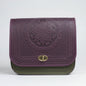 A person wearing a gray checkered coat holding a purple embossed leather crossbody purse with a geometric pattern.
