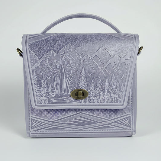 Lavender handbag with mountain design on a white brick wall background