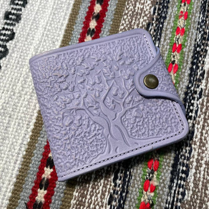 A lavender-colored, embossed leather wallet placed on a textured fabric surface.