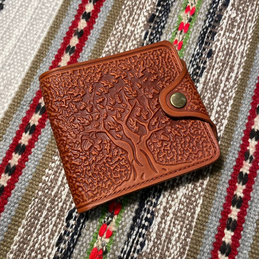 A brown wallet with embossed tree patterns on the front, placed on a striped fabric background.