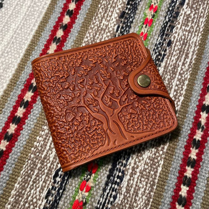 A brown wallet with embossed tree patterns on the front, placed on a striped fabric background.