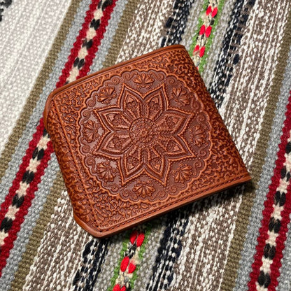 Brown leather wallet with intricate patterns on a patterned fabric background