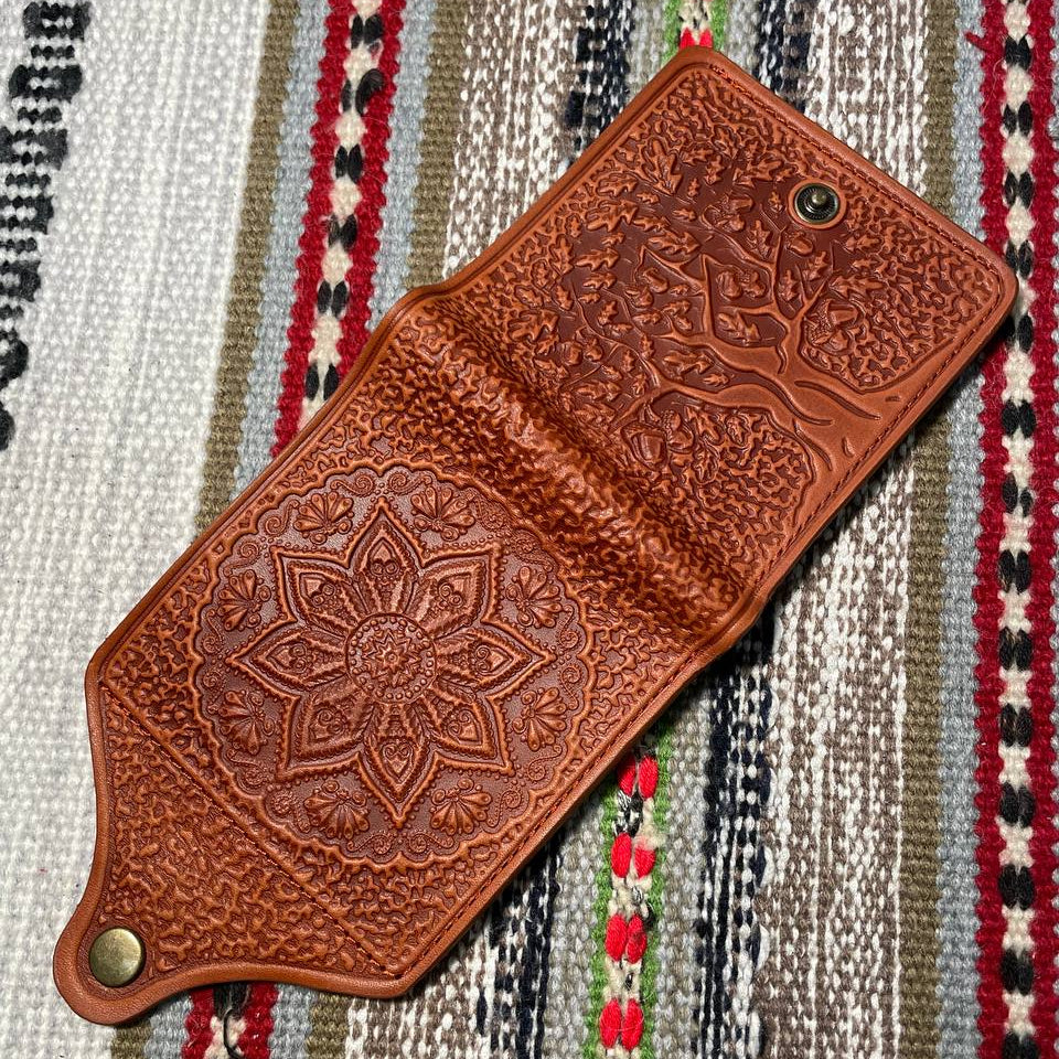 Brown leather phone case with intricate patterns on a striped fabric background