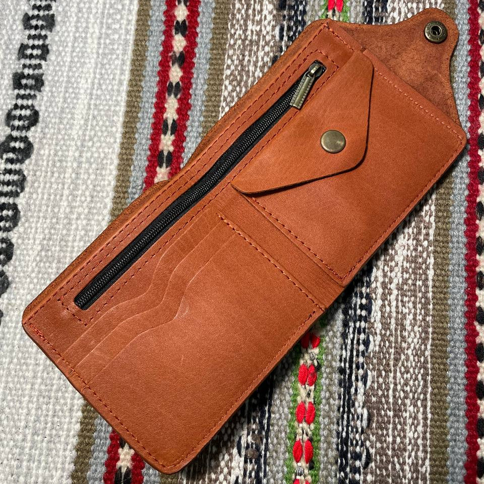 Brown leather wallet with a zipper on a patterned fabric background