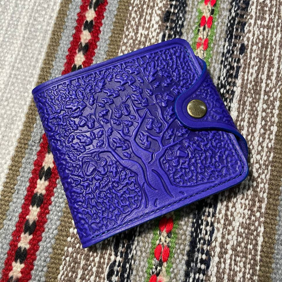 A blue leather wallet with embossed tree patterns, placed on a striped fabric surface.