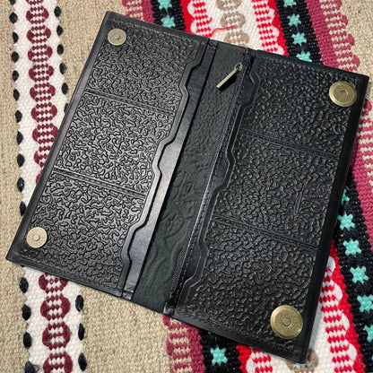 Black textured wallet with gold accents on a patterned fabric background