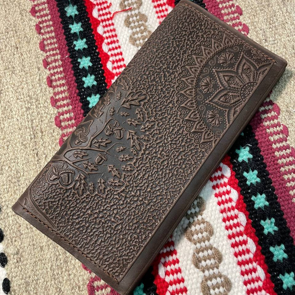 A brown wallet with embossed Tree of Life design lying on a patterned fabric.