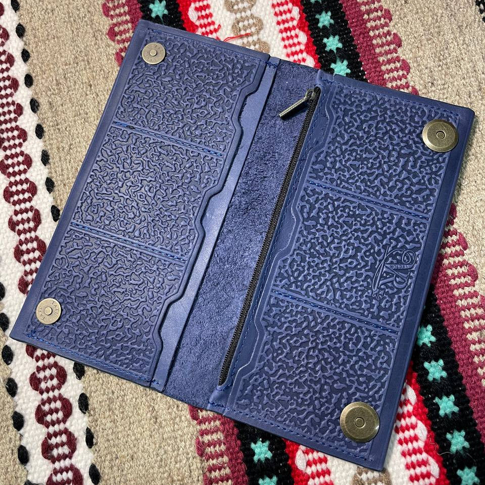 Blue textured wallet with metal buttons on a patterned fabric background