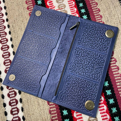 Blue textured wallet with metal buttons on a patterned fabric background