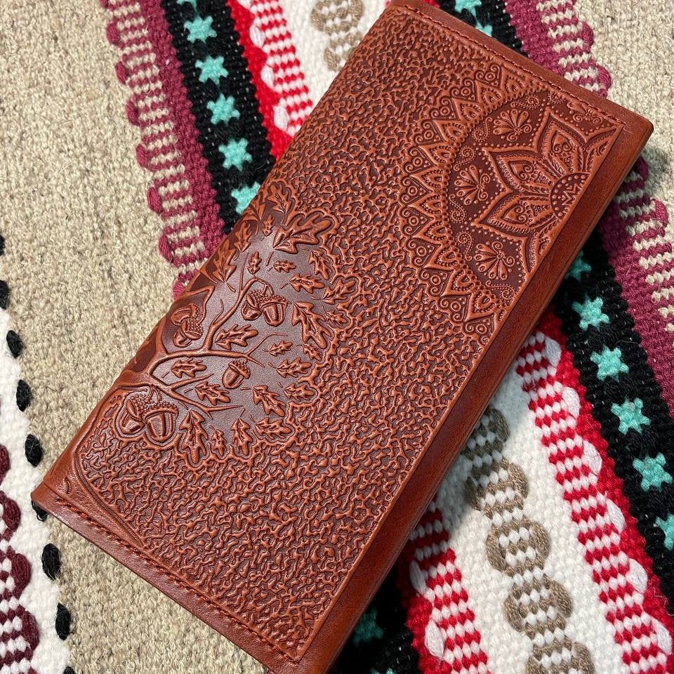 A brown wallet with embossed Tree of Life design lying on a patterned fabric.
