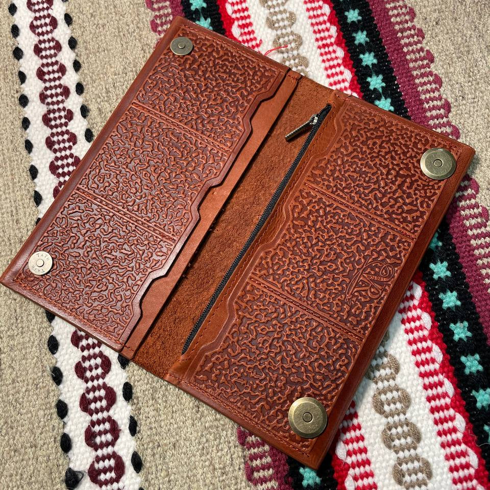 Brown leather wallet with embossed design on a colorful woven fabric background