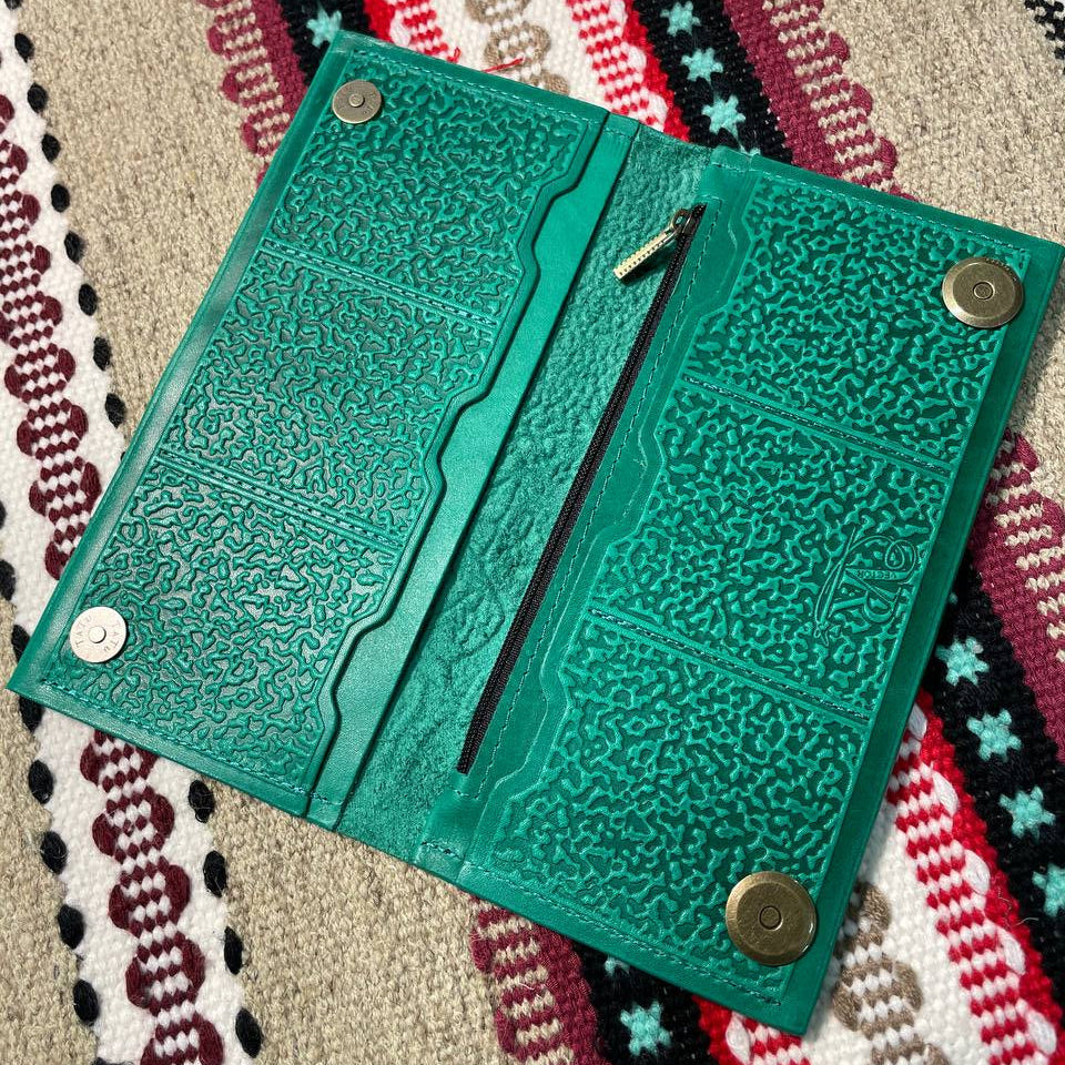 Green textured wallet with metal fastenings on a patterned fabric background