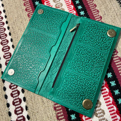 Green textured wallet with metal fastenings on a patterned fabric background