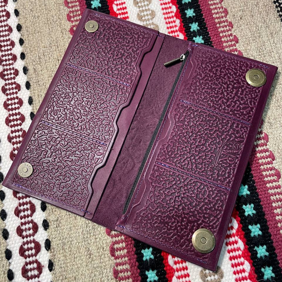 Purple leather wallet with embossed design on a patterned fabric background