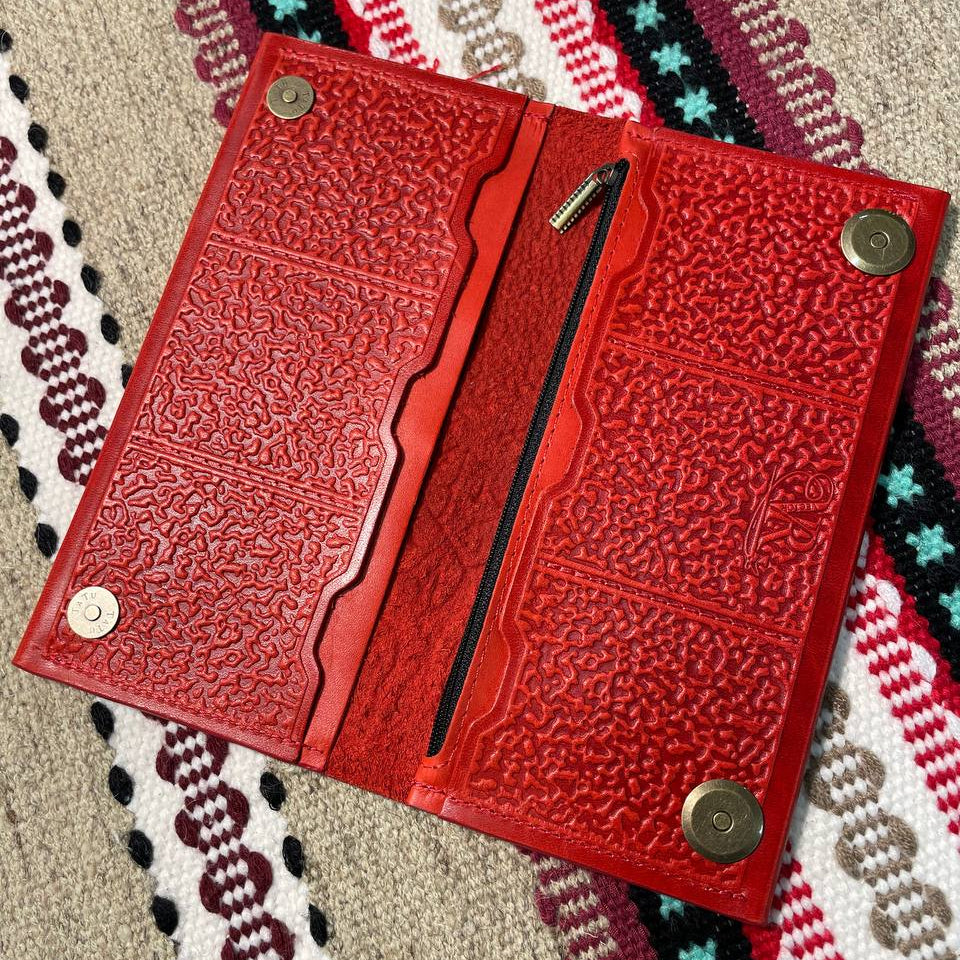 Red leather wallet with embossed design on a patterned fabric background