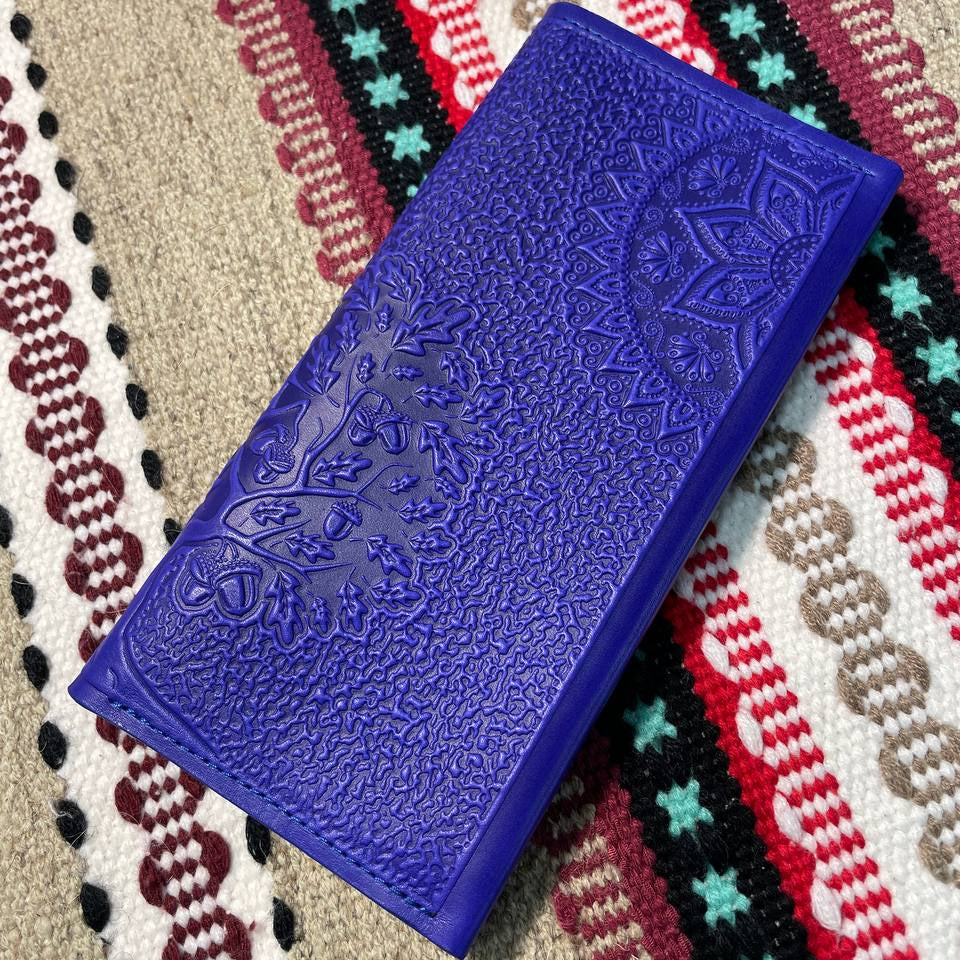 A blue wallet with embossed floral patterns on the surface, placed on a patterned fabric background.