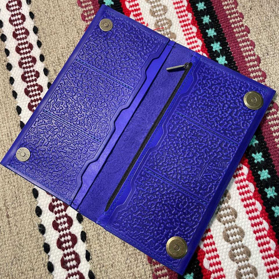 Blue textured wallet with metal fasteners on a patterned fabric background