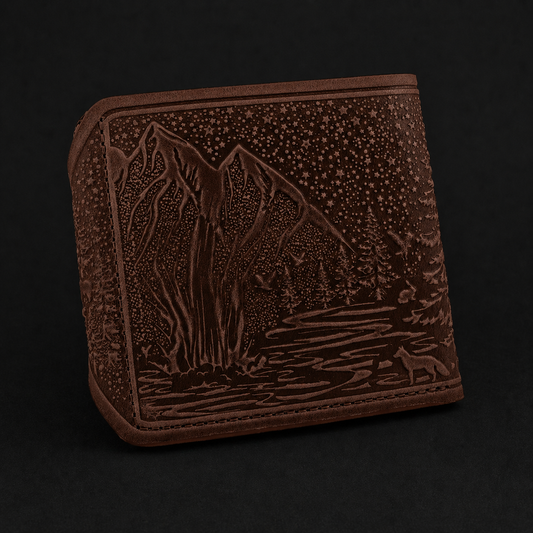 Brown leather wallet with embossed mountain and forest design on a black background