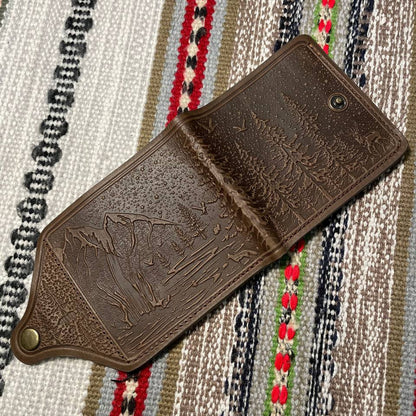 Brown leather wallet with embossed designs on a patterned fabric background