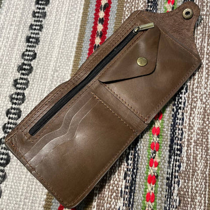 Brown leather wallet with a zipper on a patterned fabric background