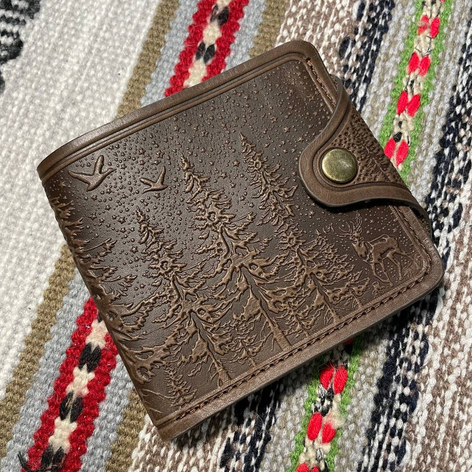 A brown wallet with embossed leather texture and a decorative element in the center, placed on a patterned fabric.
