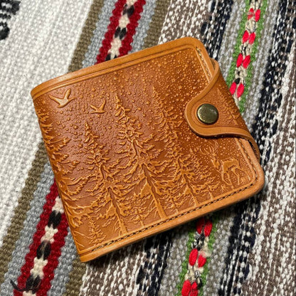 A brown wallet with embossed pattern on the front, placed on a patterned fabric surface.