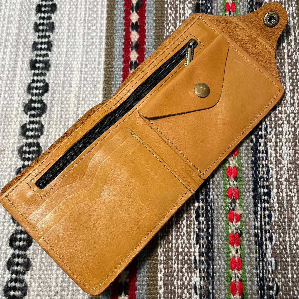 Brown leather wallet with a zipper on a patterned fabric background