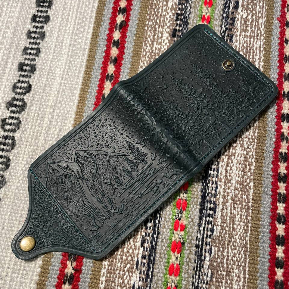 Dark green leather wallet with embossed design on a patterned fabric background