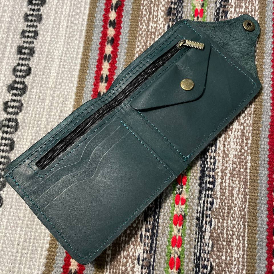 Green leather wallet with a zipper on a patterned fabric background