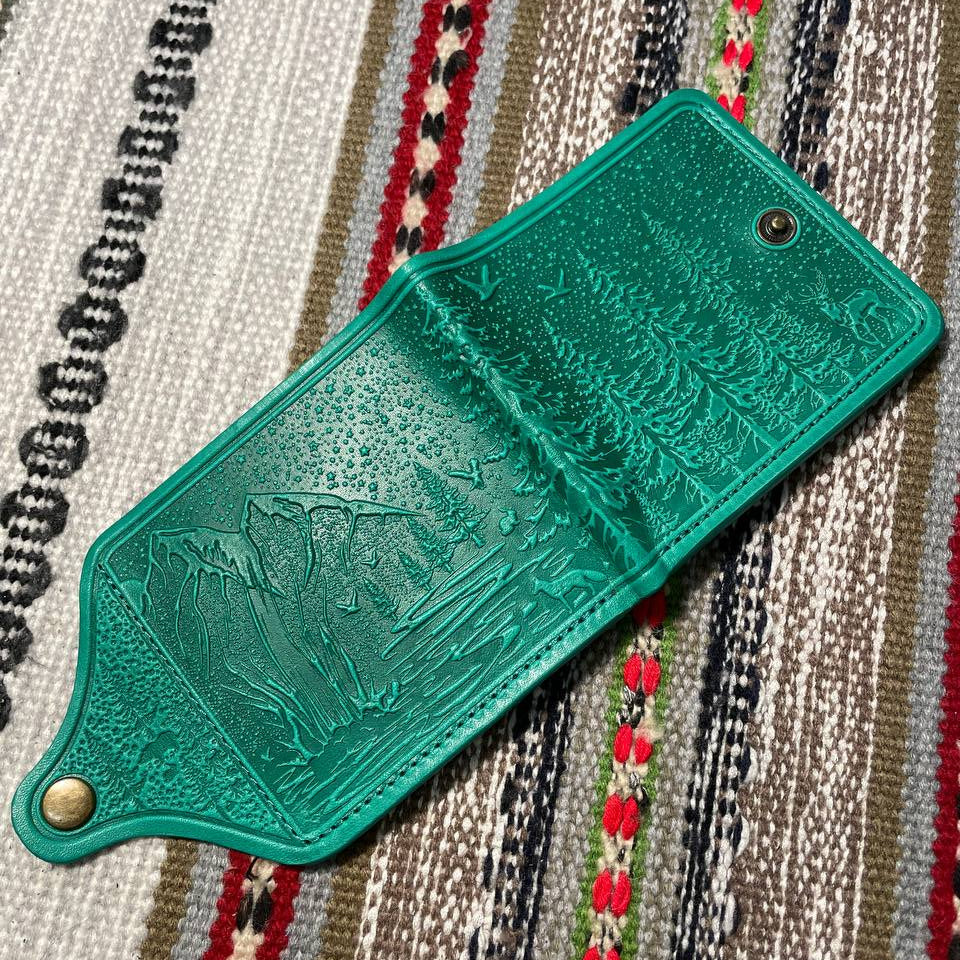 Green leather wallet with embossed design on a patterned fabric background