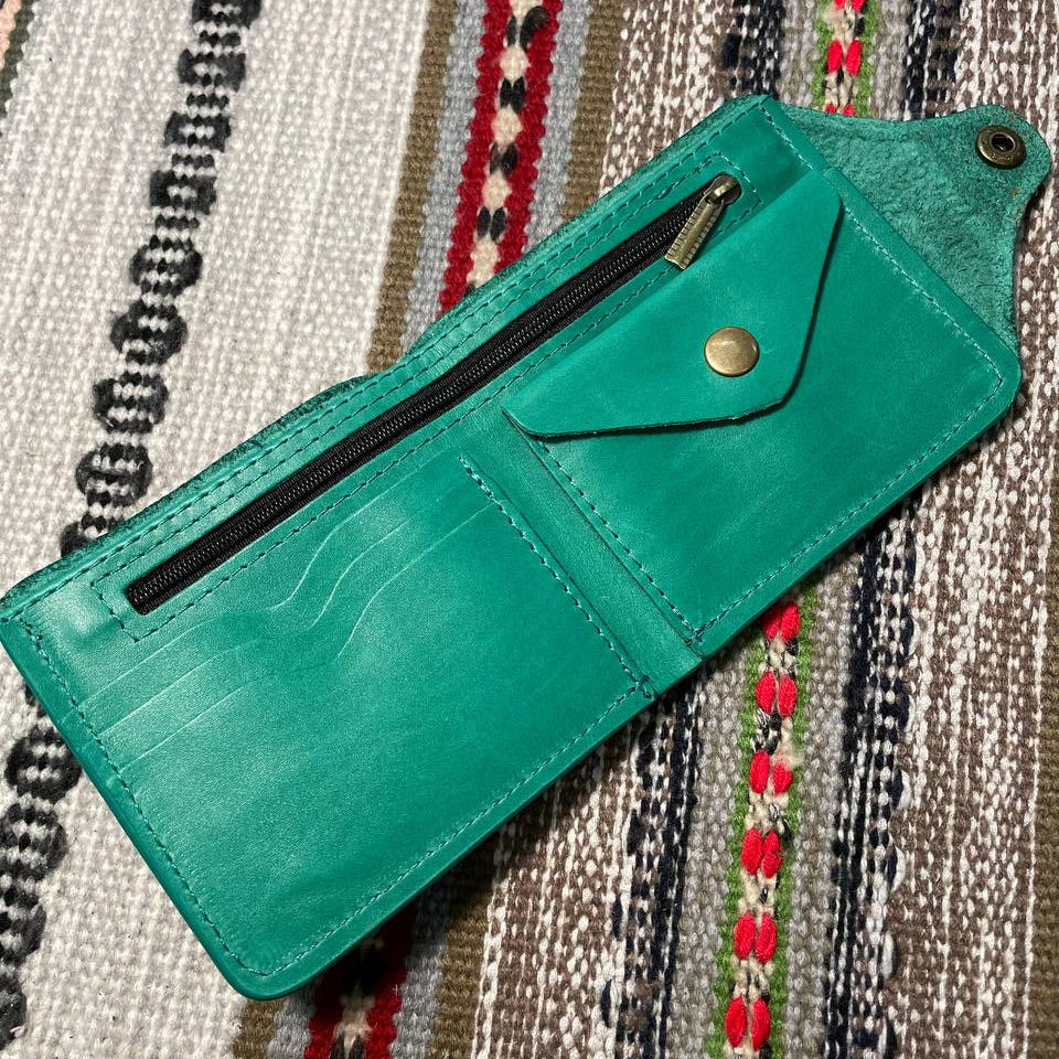 Teal leather wallet with a zipper on a patterned fabric background