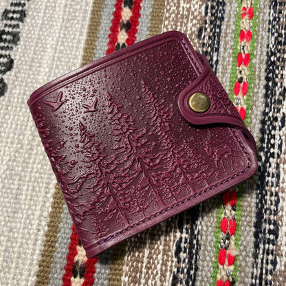 A purple wallet with embossed floral patterns on it, placed on a patterned fabric surface.