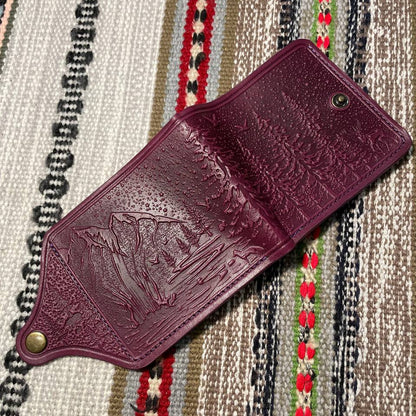 Purple leather wallet with embossed design on a patterned fabric background