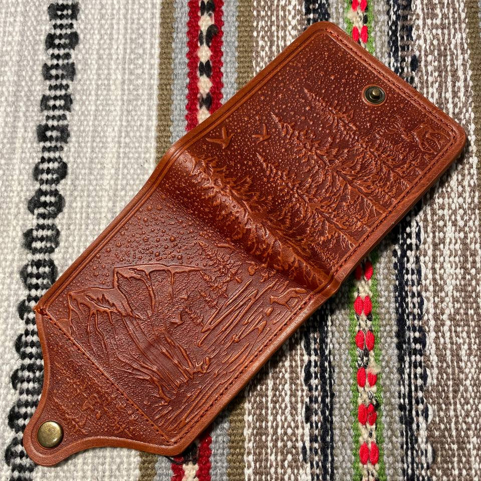 Brown leather wallet with embossed design on a patterned fabric background