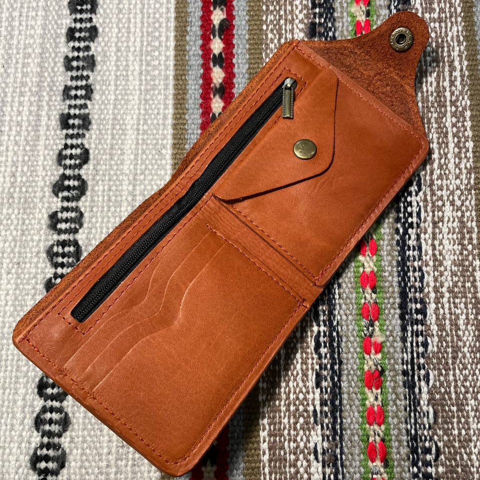 Brown leather wallet with a zipper on a patterned fabric background