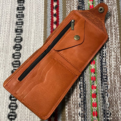 Brown leather wallet with a zipper on a patterned fabric background
