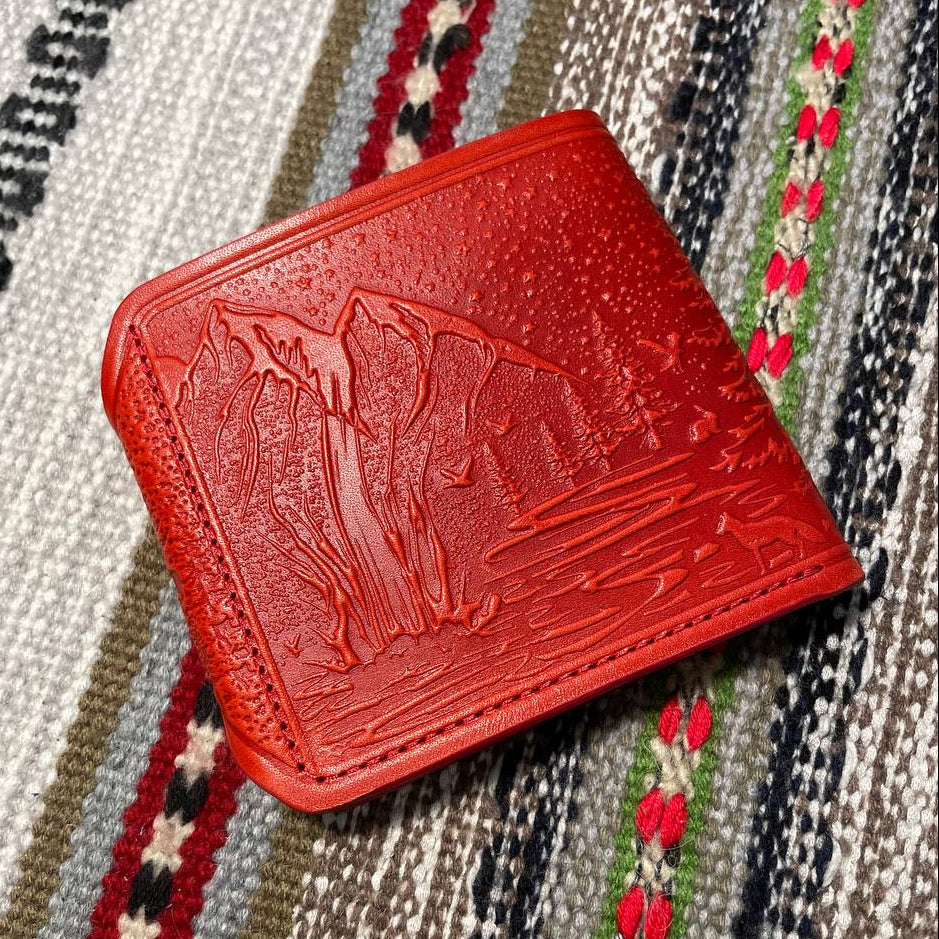 Red leather wallet with embossed design on a patterned fabric background