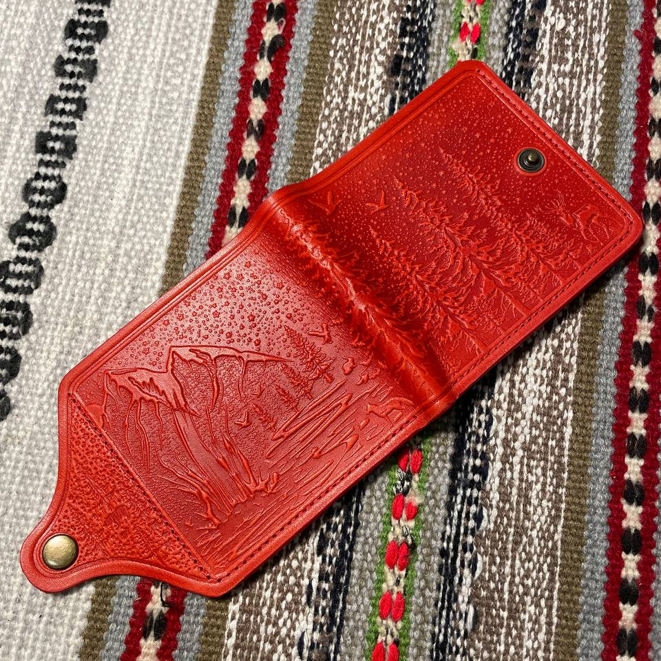 Red leather wallet with embossed design on a striped fabric background