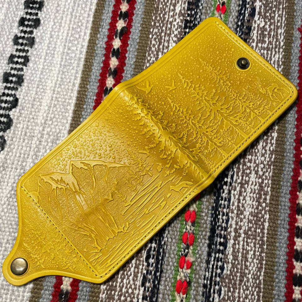 Yellow leather wallet with embossed design on a patterned fabric background